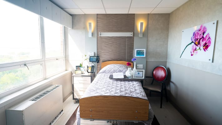 Well-lit private resident room with a bed and chair