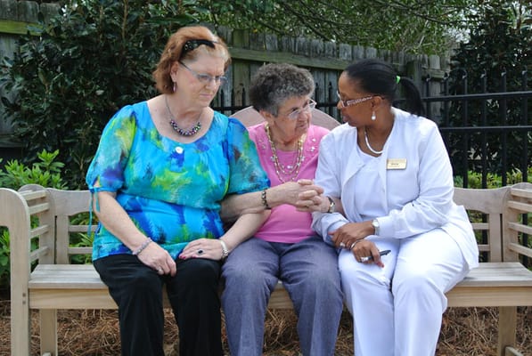 Three women sitting on a bench outdoors, talking intimately