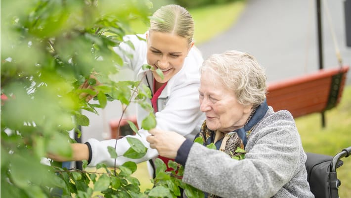 Caregiver assisting a resident outdoors with plants
