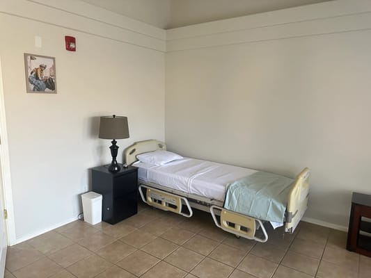 A well-furnished patient bedroom with a bed, lamp, and nightstand.