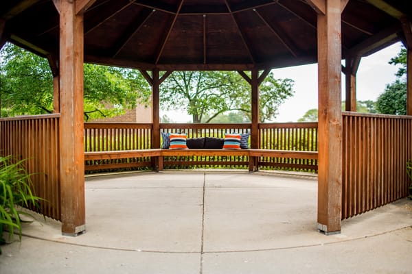 A gazebo with benches and cushions in a garden