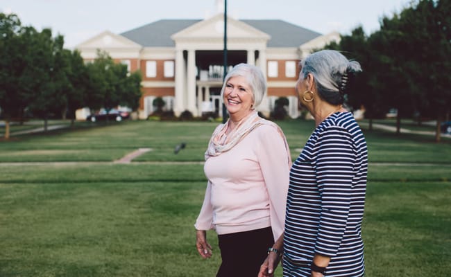 Two women walking outdoors in front of a senior living facility