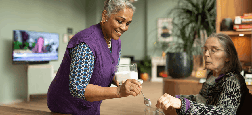Staff assisting resident with a drink in an interior space