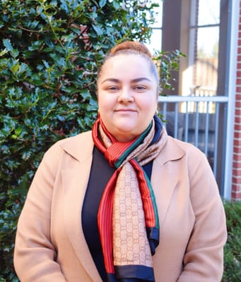 A staff member posing outside, surrounded by greenery