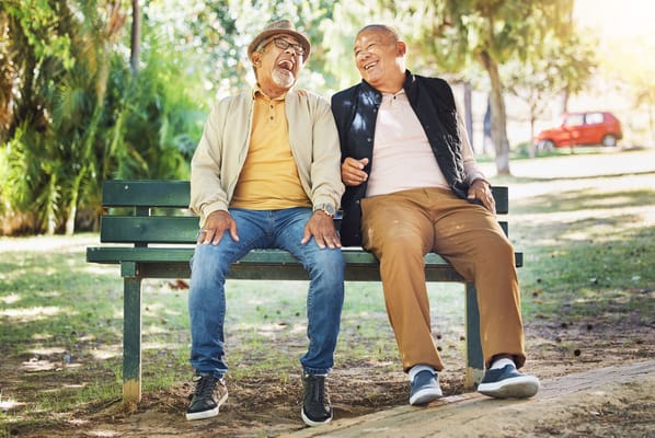 Two seniors laughing on a bench in a park