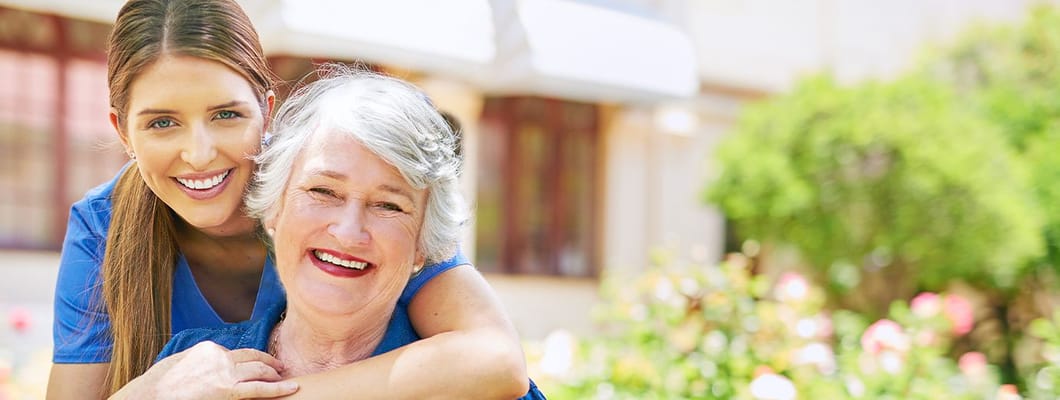 A caregiver embracing a smiling resident in a garden