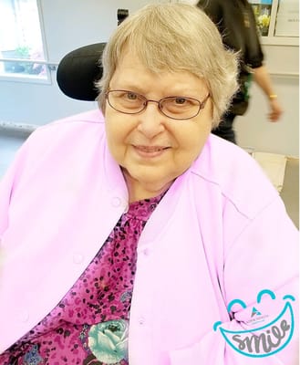 Smiling resident in a common area wearing a pink cardigan