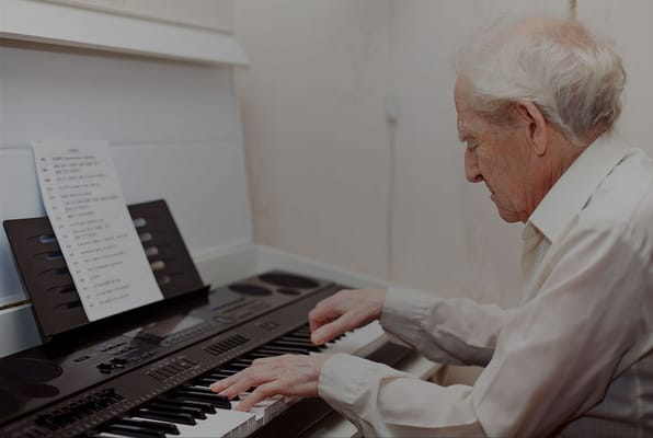 An elderly man playing keyboard in a facility room