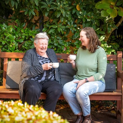 Two women enjoying tea on a garden bench