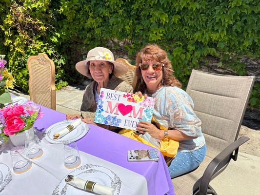 Two women celebrating with a sign in an outdoor setting