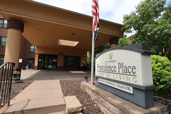 Main entrance of Providence Place Senior Living with sign and flag