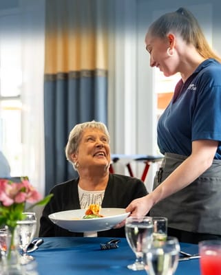Resident enjoying meal served by staff in dining room