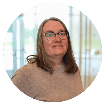 A woman with glasses smiling in a bright interior space