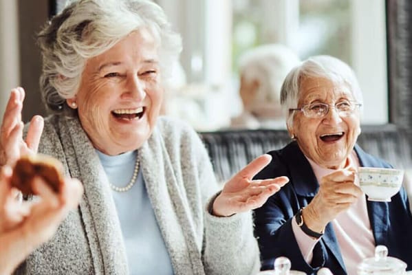 Two smiling elderly women enjoying tea together