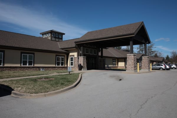 Front entrance of a senior living facility with a canopy and parking area.