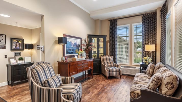 Cozy living room with two armchairs and a sofa, decorated with curtains and lamps.