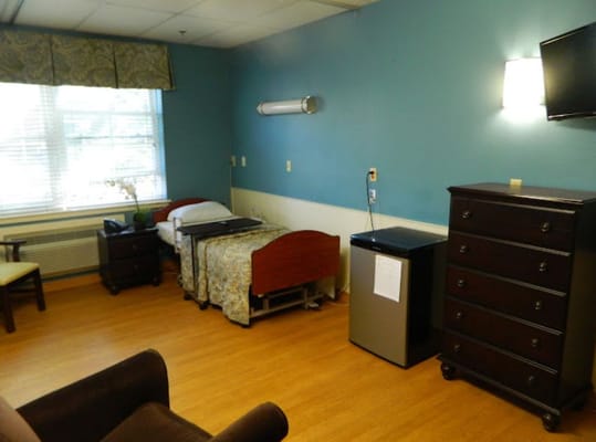 Interior view of a resident room featuring a bed, dresser, and seating area.