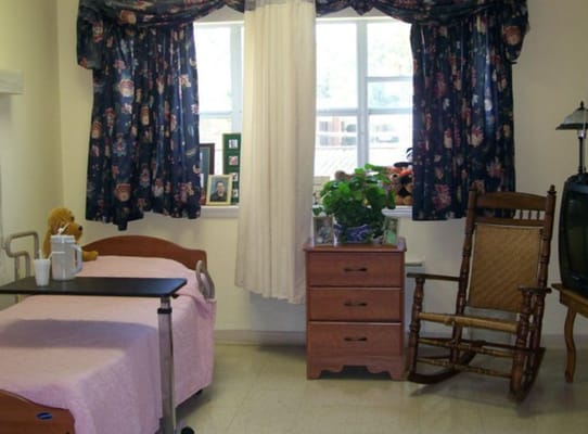 A cozy nursing home room with a bed, rocking chair, and personal touches.