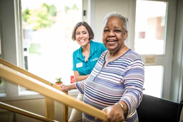 A staff member assisting a smiling resident indoors