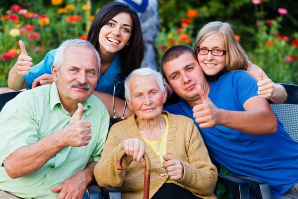 Group of seniors and caregivers giving thumbs up in garden.