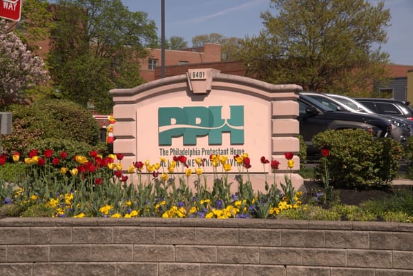 Sign for The Philadelphia Protestant Home surrounded by colorful flowers