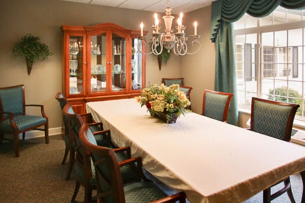 A spacious dining room with a long table, decorative chairs, and a chandelier.