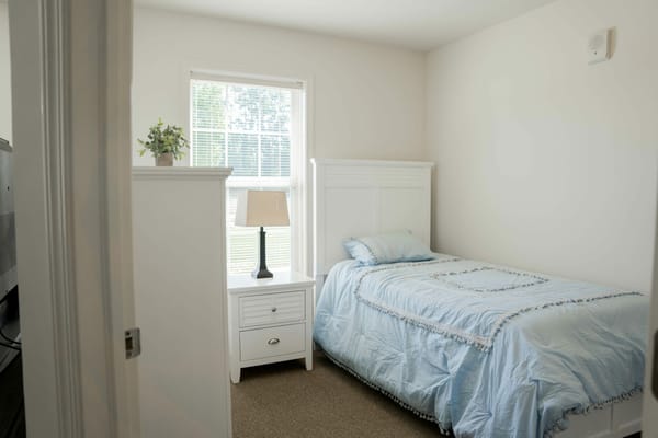 A bright bedroom with a bed, lamp, and window.