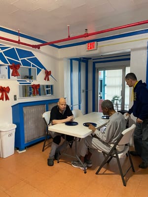Two residents seated at a table with plates, one resident standing nearby