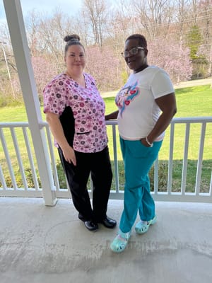 Two staff members standing on a porch with greenery in the background