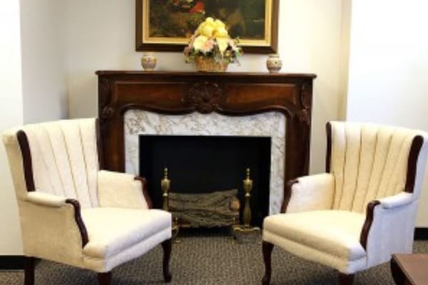 Two plush chairs in a living room with a fireplace and floral arrangement