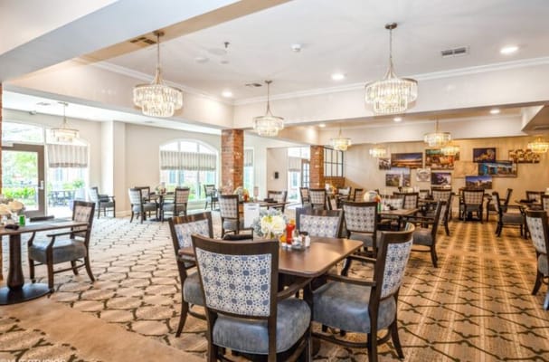 Bright dining area with elegant chandeliers and tables set for residents.