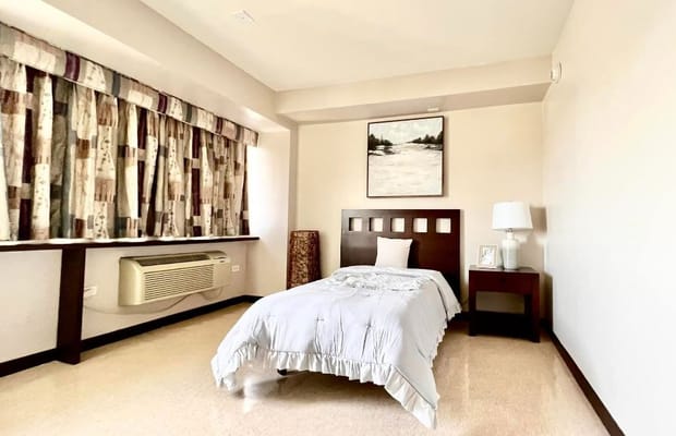 A cozy bedroom featuring a single bed, bedside table, and air conditioning unit.