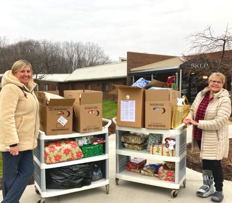 Two staff members beside carts filled with holiday gifts and food items.