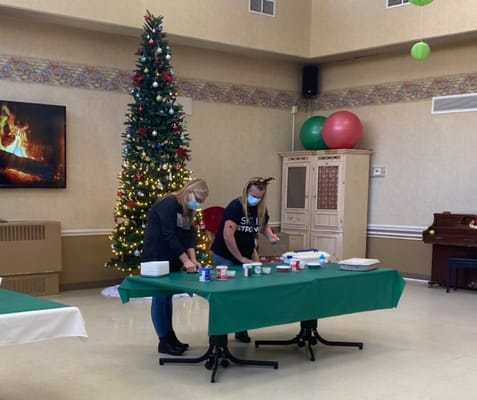 Two staff members prepare for a holiday activity in front of a Christmas tree.