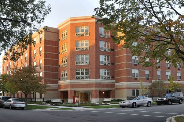 Exterior view of a senior living facility with trees and cars
