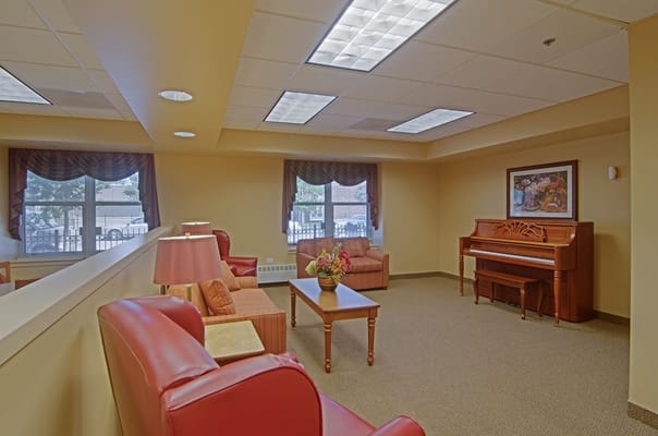 Cozy lounge area with piano and seating at Senior Suites of Marquette Village