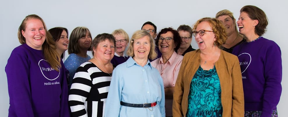A joyful group of women, some in Seurana Oy sweaters, smiling together.