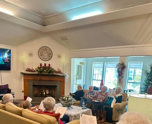 Seniors sitting together in a festive lounge, singing and sharing music sheets.
