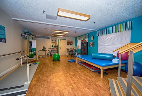 A therapy room with exercise equipment and various colorful exercise balls.