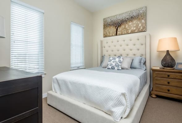 A well-furnished bedroom with a bed, bedside table, and windows.