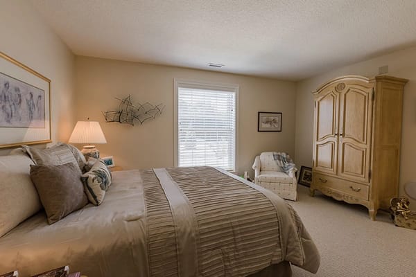 Brightly lit private bedroom with a bed, chair, and wardrobe.