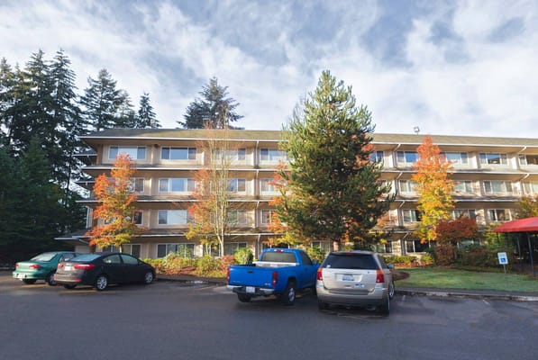 A three-story building surrounded by autumn trees and parked cars.