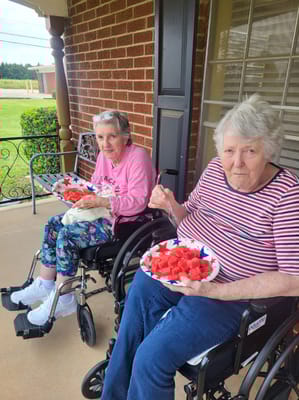 Two residents enjoying watermelon outside on a porch