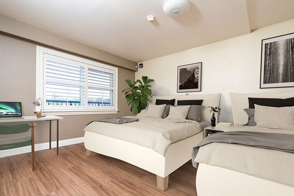 A well-furnished dual bedroom with two beds, a desk, and decorative plant.