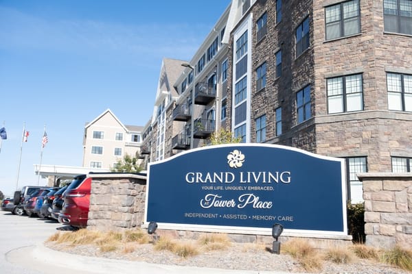 Sign for Grand Living at Tower Place with residential building in the background.