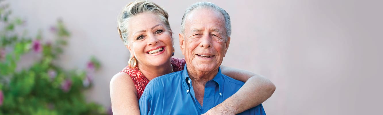 A smiling woman hugging an elderly man outdoors
