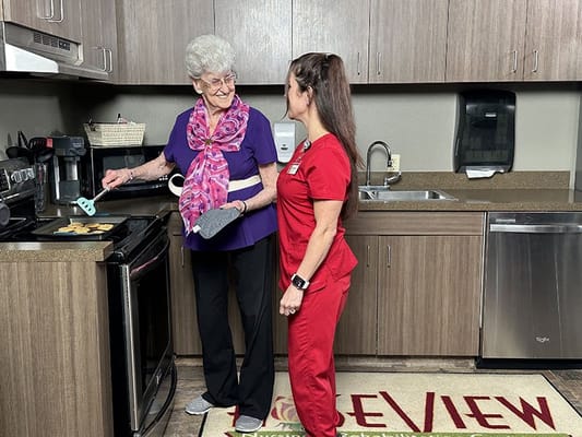 A resident and staff member baking cookies in a kitchen