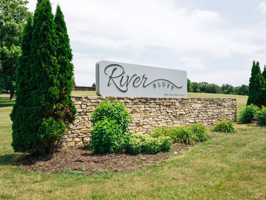 Sign for River Bluff Nursing Home surrounded by greenery