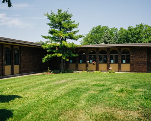 Sunny exterior view of River Bluff Nursing Home with green lawn and trees.