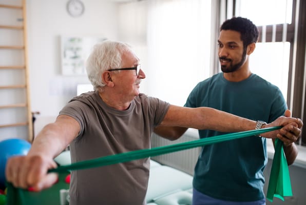 A senior man exercising with a trainer using resistance bands.